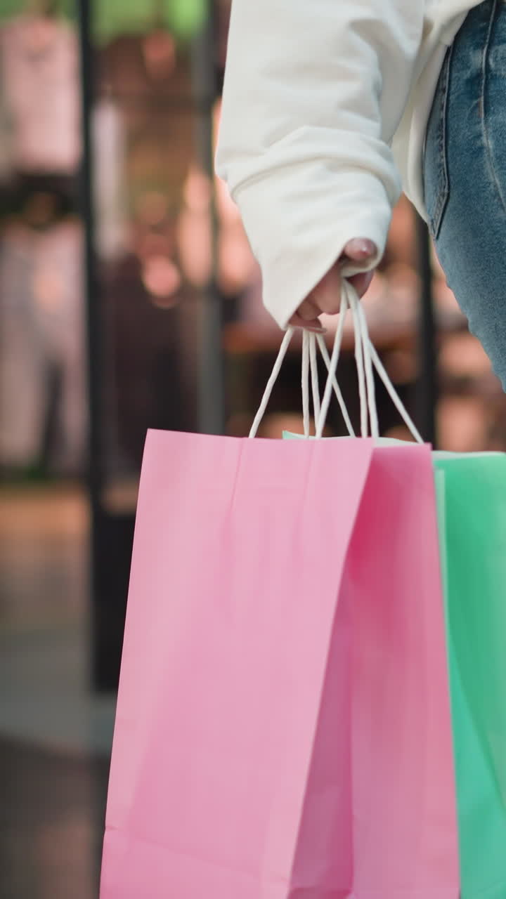 백색 과 청바지를 입은 쇼핑객이 핑크색과 민트색 쇼핑백을 들고 남녀를 위한 흐릿한 옷을 가진 옷 가게를 탐험하는 모습