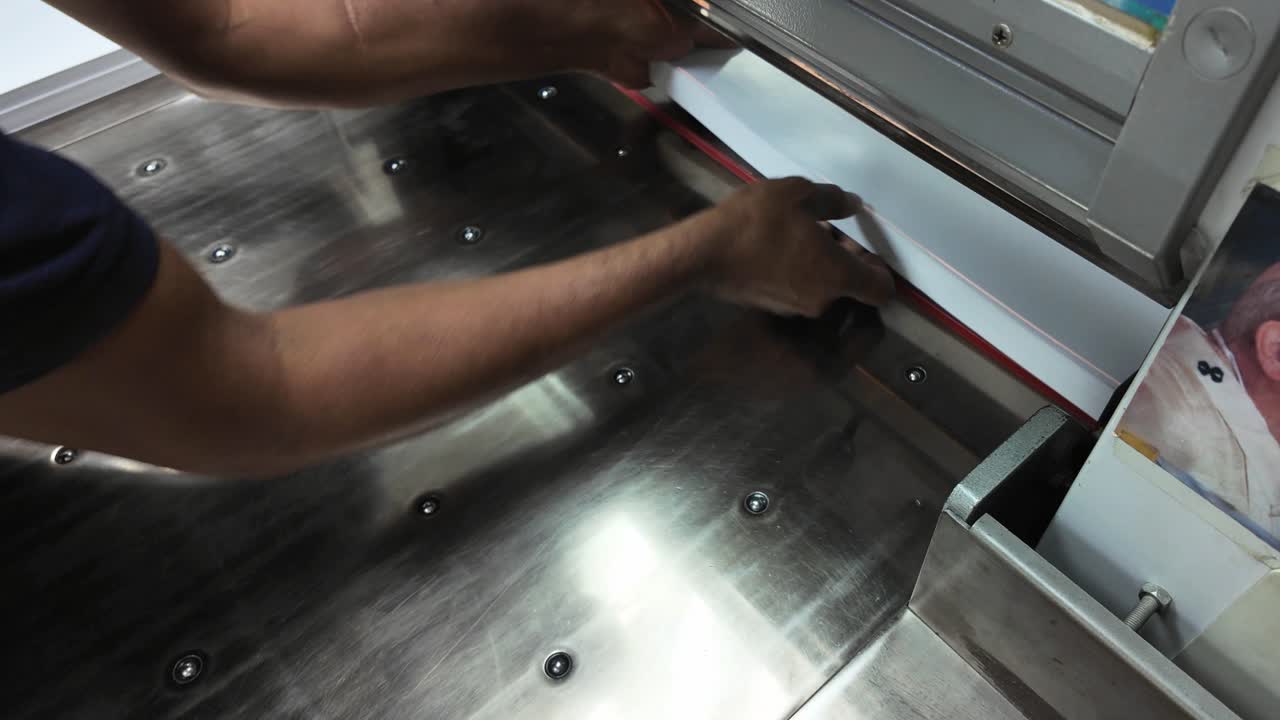 A skilled operator expertly trims a stack of paper using a guillotine in a lithographic printing environment. The precision ensures quality and clean edges, vital for print production.