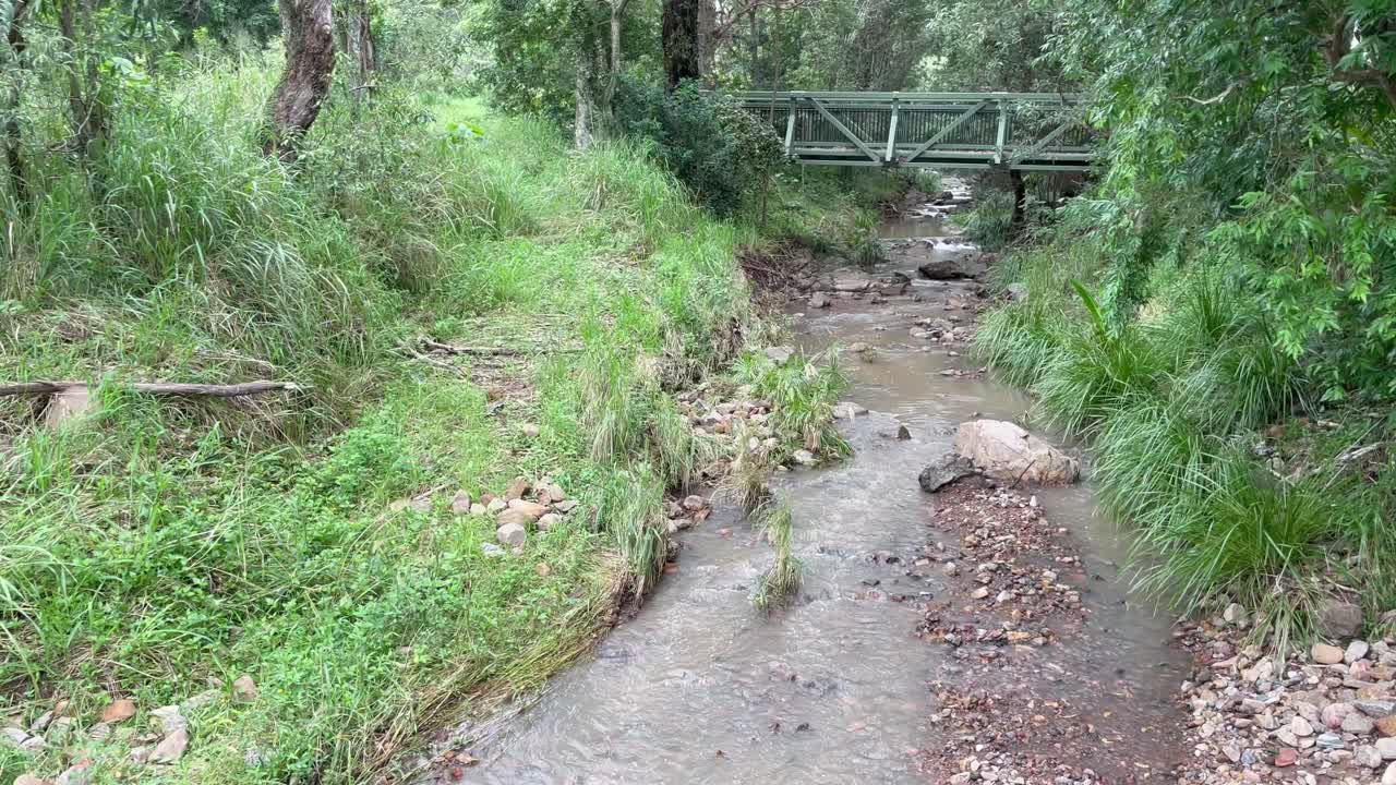 4K Video of a small creek becoming muddy after rain with a bridge in the background in Australia