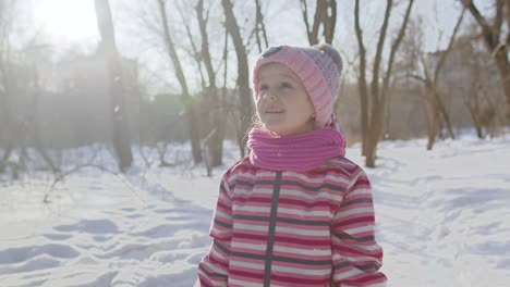 cheerful child girl walking on snowy road in winter sunny park forest, christmas holidays traveling