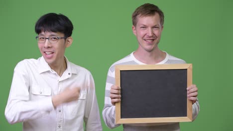 two happy young multi-ethnic businessmen showing blackboard and giving thumbs up