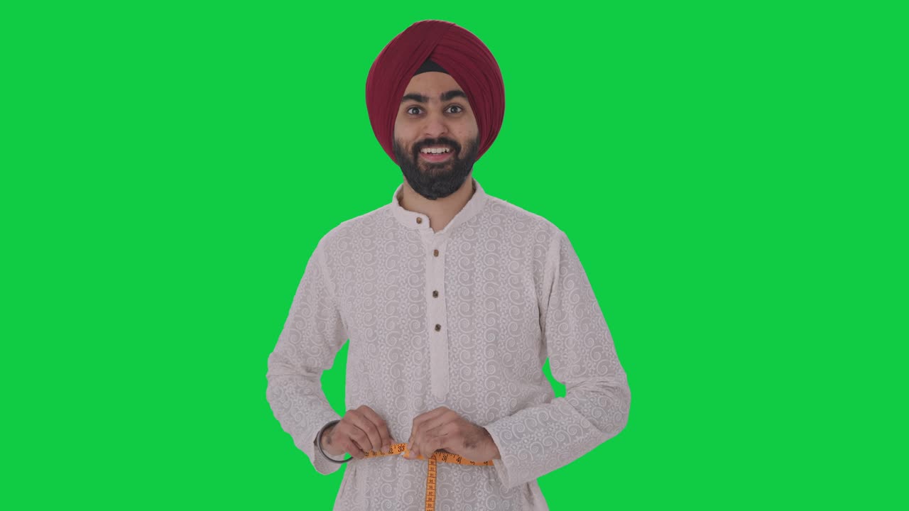 Uomo indiano Sikh felice che misura la vita con un metro a nastro, schermo verde.