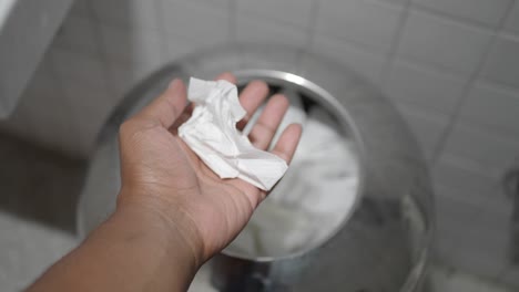 hand reaching into a trash can with tissue paper