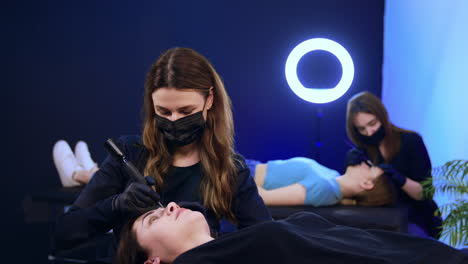 salon brow masters performing permanent brow make up to the clients. beauty professionals work in masks.