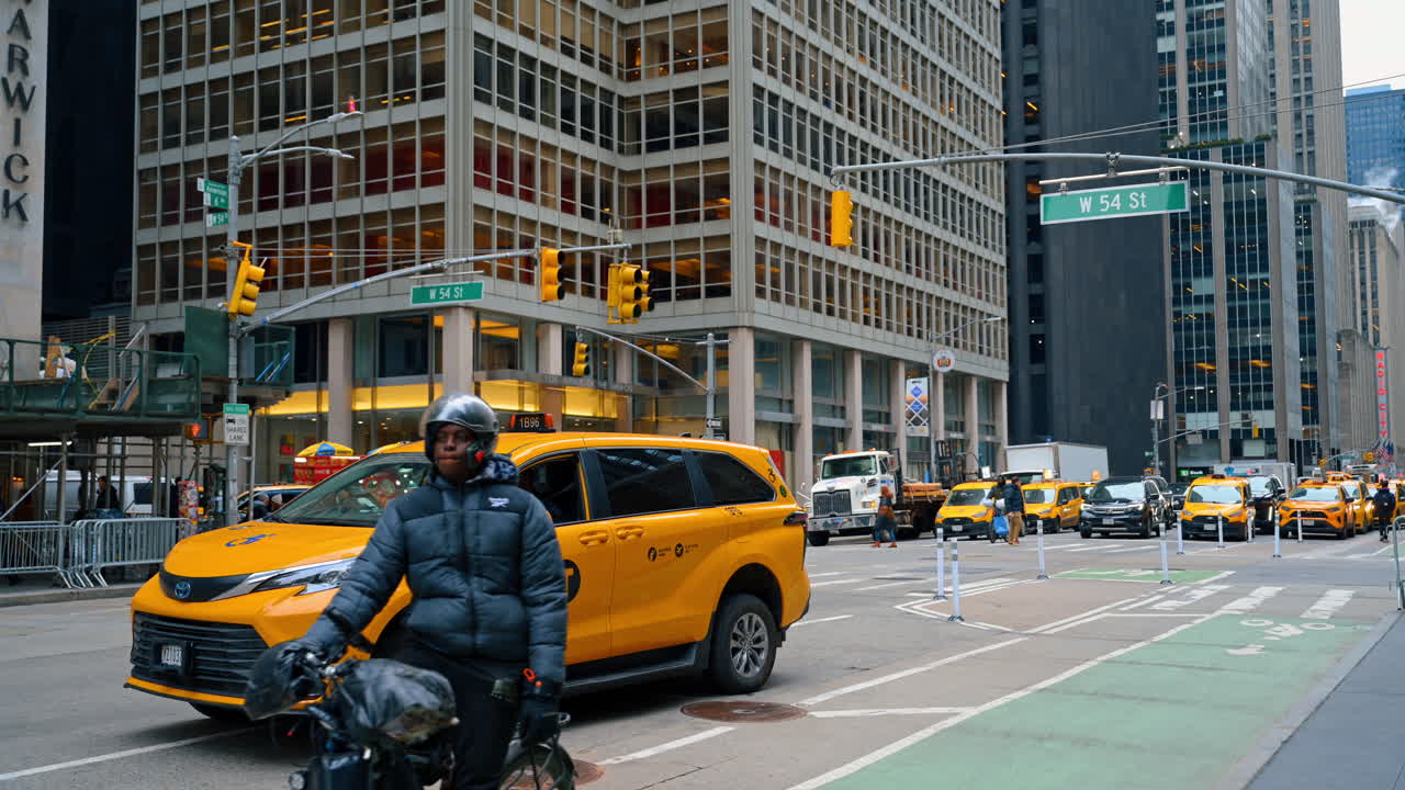 New York, USA, 8. april 2026: Gul taxa og cyklist ved krydset West 54th Street. Gul Toyota taxa og budcyklist på et gadehjørne med New York City trafikskilte og skyskrabere