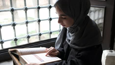 hijab girl reciting the quran by the window