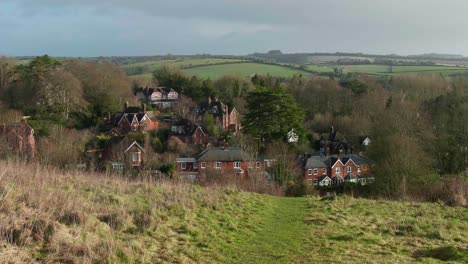 a woman hikes from hilltop towards a beautiful village nestled in rolling hills, forests and national park in background