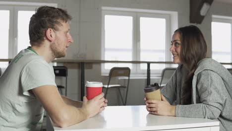 Two-friends-are-sitting-at-the-table-in-cafe,-drinking-coffee-to-go-in-paper-cups-and-talking.-Shot-in-4k