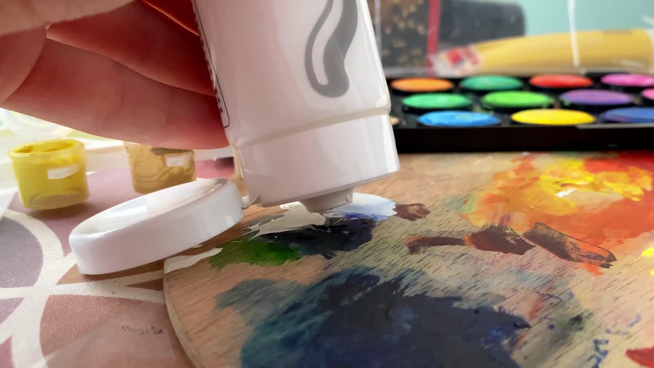 Close up shot of an artist's hand applying white color from painting tube onto a wooden palette