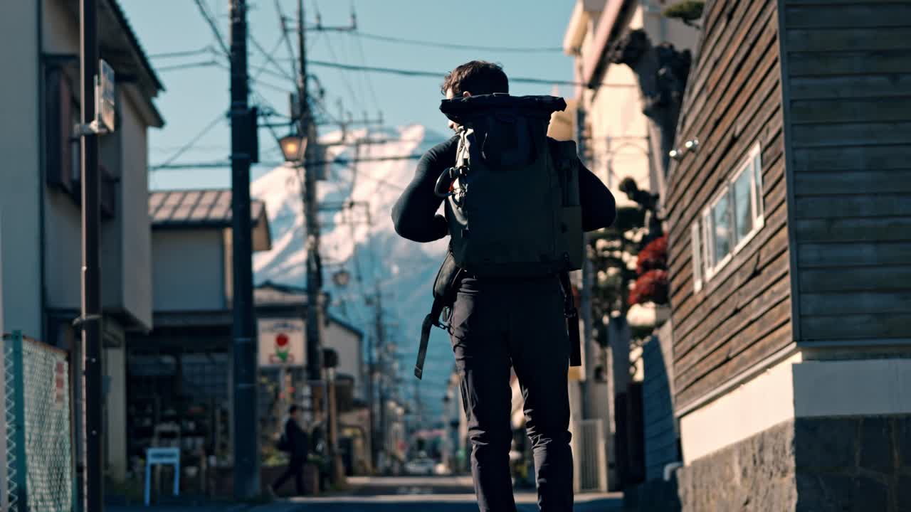 This cinematic video clip features a backpacker strolling through a street in Shizuoka City, with the majestic, snow-covered Mount Fuji in the backdrop.