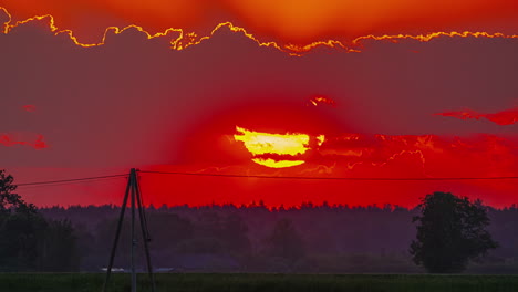 intenso amanecer rojo sobre un horizonte lejano con un paisaje siluetado de árboles de hoja perenne y líneas eléctricas