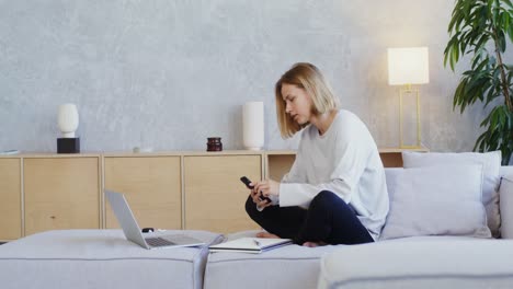 mujer trabajando desde casa en un sofá con portátil y teléfono
