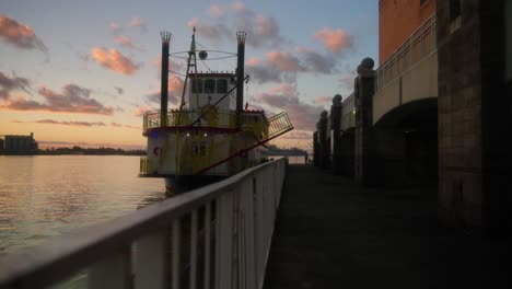 steamboat ferry docked on water at sunset with beautiful clouds in mobile, alabama at port panning right slow motion in 4k with fence in foreground