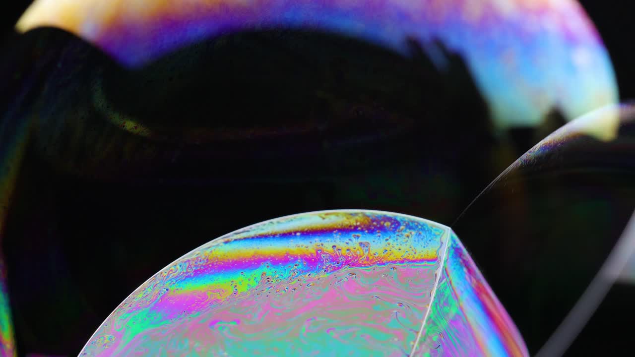 Vibrant soap bubble displays shifting colors and reflections against a dark background, capturing dynamic light play and fluid motion