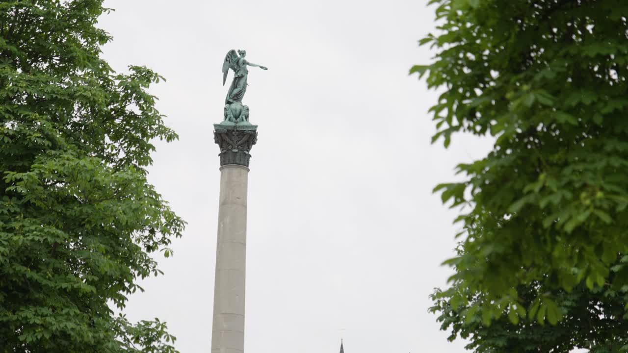 статуя jubiläumssäule на юбилейной колонне в штутгарте, германия, статическая с облачным небом и ветреными листьями на зеленых деревьях вокруг