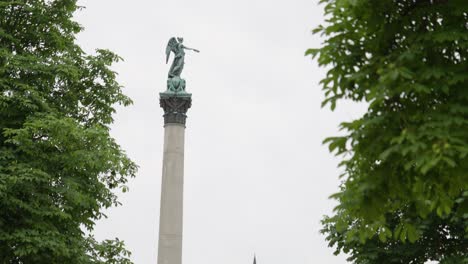 Jubiläumssäule-Statue-at-Jubilee-Column-in-Stuttgart,-Germany,-static-with-cloudy-sky-and-windy-leaves-on-green-trees-around