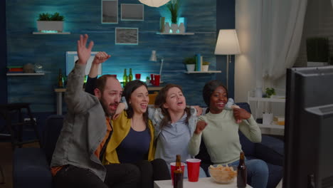 group of multiracial people cheering football team while sitting on couch