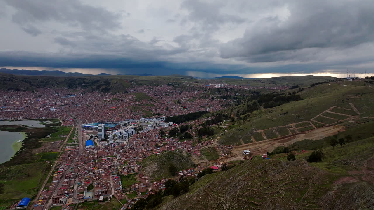 Aerial drone view of Puno city sprawling across the hills next to Lake Titicaca. Dense urban landscape with red roofs under a cloudy sky in the Peruvian Andes