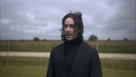 young, religious man in black suit worshipping and praying in front of christian cross