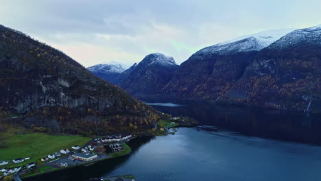 Fiordo-Aéreo-Con-Un-Pequeño-Pueblo-En-La-Costa-Y-Picos-Nevados-En-El-Fondo