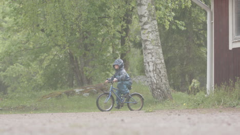 slow motion - a young child riding their bike in heavy rainfall