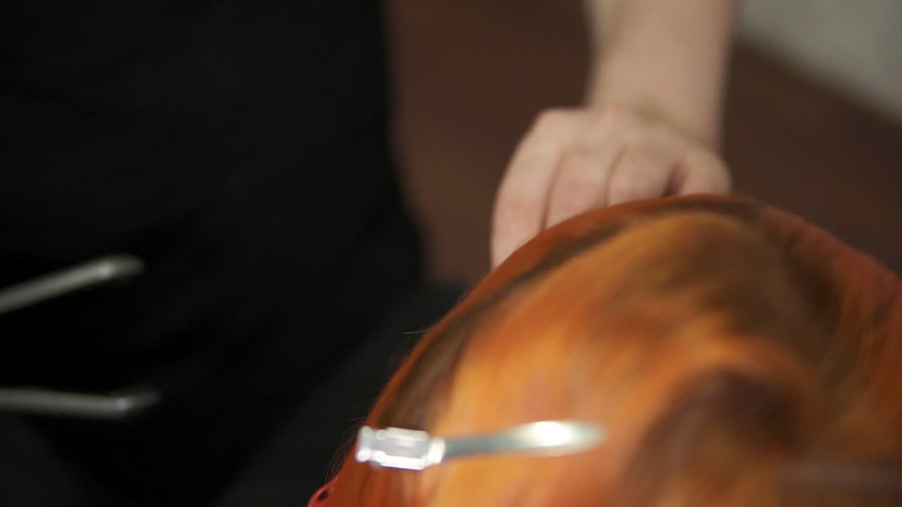 Close Up view of redhead woman's hair being straightened by a professional hair stylist using a hairstraightener in hair salon