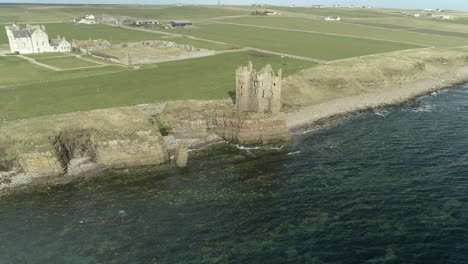 Aerial-shot-tracking-left-to-right-and-circling-Keiss-Castle-on-a-sunny-day,-Caithness,-Scotland