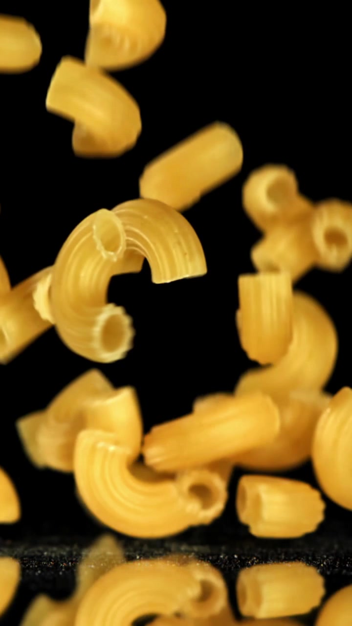 Maccheroni secchi che cadono al rallentatore su una superficie nera riflettente