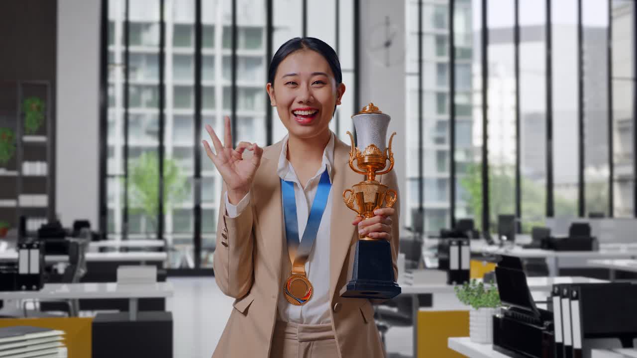 Asian Business Woman In A Suit With A Gold Medal And Trophy Showing Okay Gesture And Smiling To Camera As The First Winner In The Office