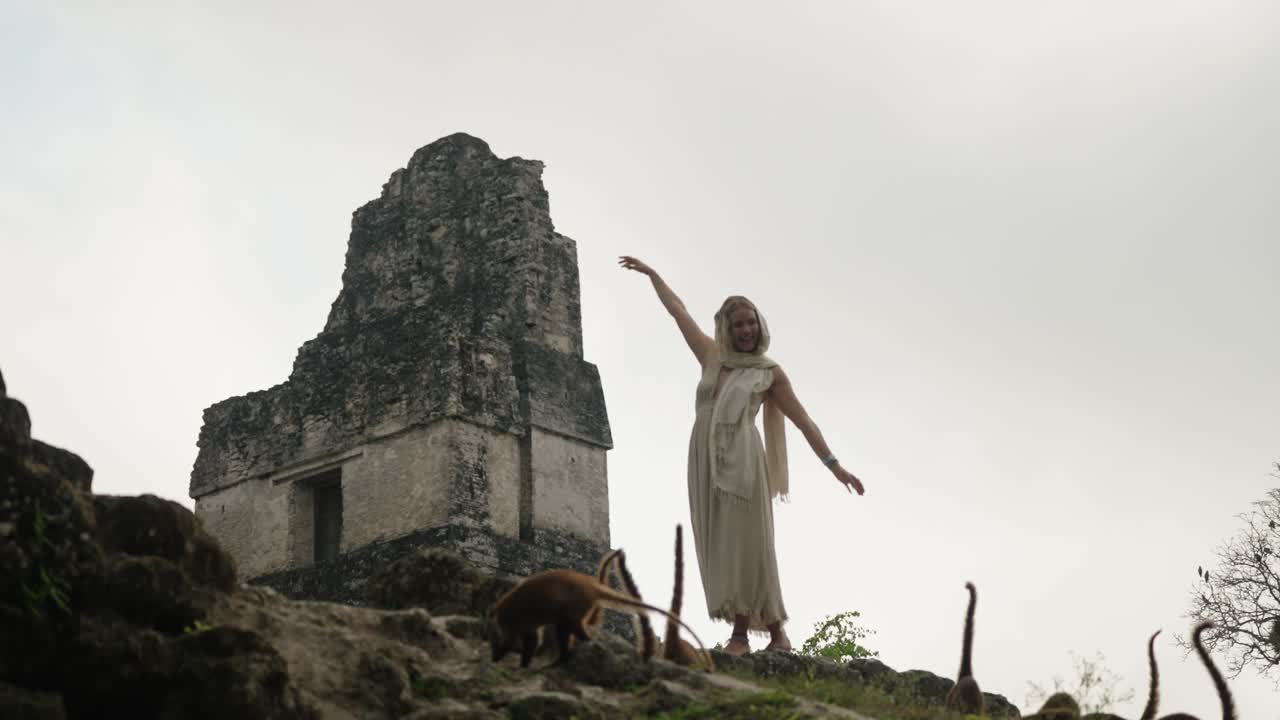 A woman walks among coatis near Temple II, an ancient Mayan pyramid in the Tikal National Park, Petén, Guatemala.