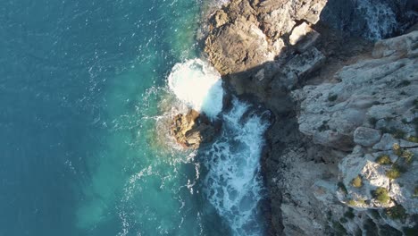 Antenne-Mit-Blick-Auf-Wellen,-Die-Auf-Felsen-In-Cala-Llonga,-Ibiza,-Krachen