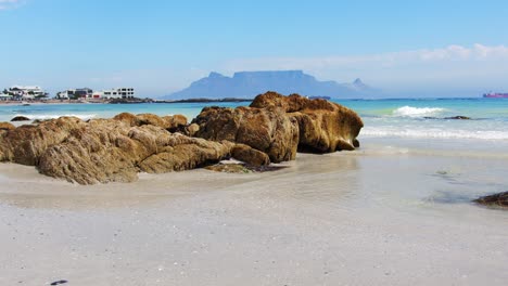 slow pan across the white sand beach and rocks, with table mountain cape town in background