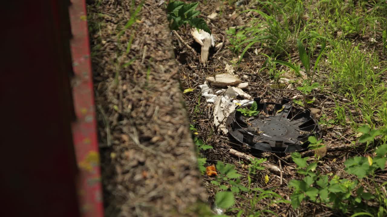 la tapa del cubo se sienta en el lado del hombro de hierba detrás de la valla oxidada por la carretera