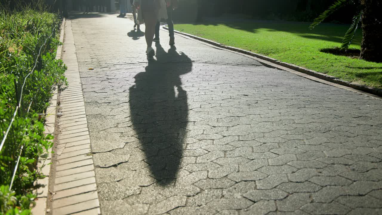 Diverse pedestrians entering from far end, walking toward camera on paved park path, long shadows