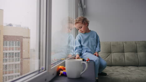 little boy is boring alone in room looking out window in snowy day orphan child in children shelter