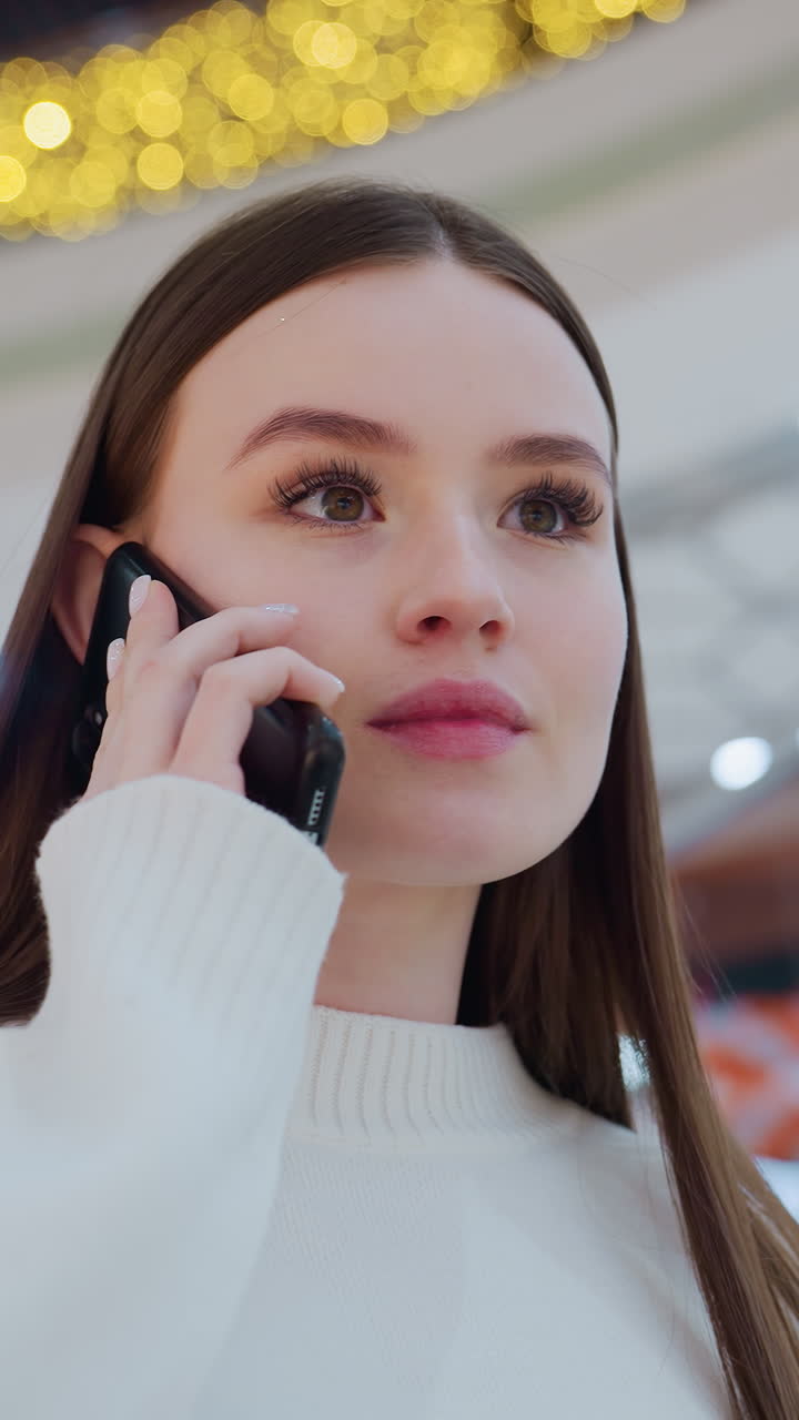 Confident young woman talking on phone while ascending escalator in stylish shopping mall, bright interior, elegant design, and warm lighting create a modern