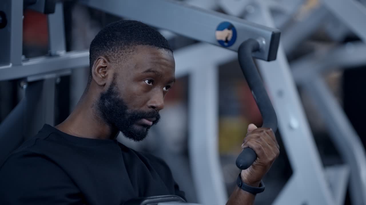 An athletic black man performs one armed lat pull down