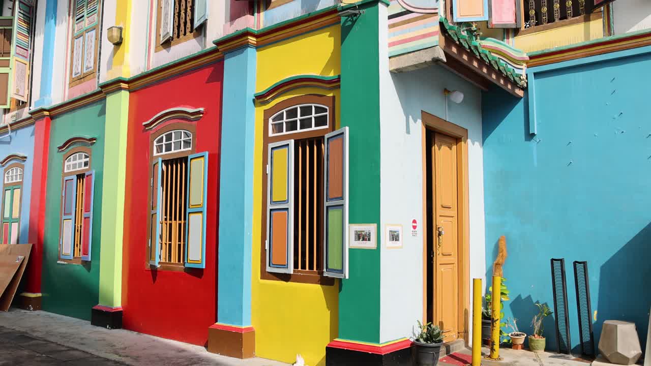 Colorful heritage shophouse facade with ornate windows, upward pan in bright daylight, urban street