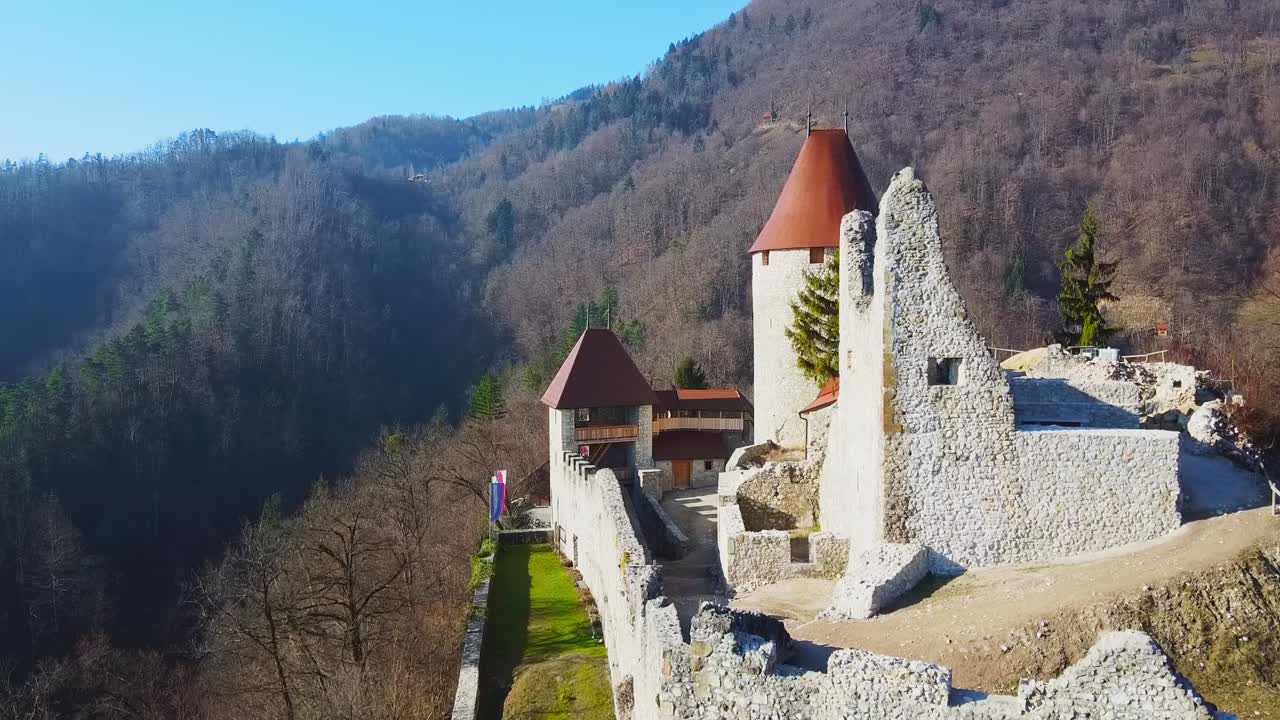 Aerial rising shot of medieval stronghold in Slovenia known as Zovnek castle, near Braslovce village, with mountainous landscape covered with forest in the distance