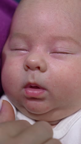 face of an infant baby sleeping deeply and doesn't want to wake up. loving mum trying to wake her kid up and touches his sweet cheeks tenderly. close up. vertical video
