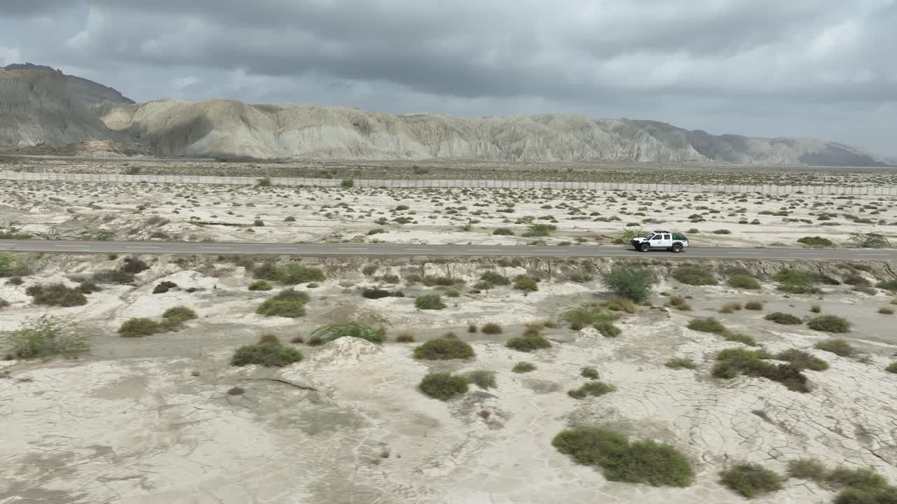 공중 드론 은 구름 이 많은 날 에 발로치스탄 의 힌골 국립 공원 을 가로지르는 고속도로 도로 를 따라 운전 하는 자동차 를  ⁇ 고 있다