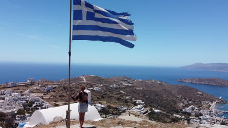 vista aérea desde la cima de la isla ios en grecia, mujer y bandera griega