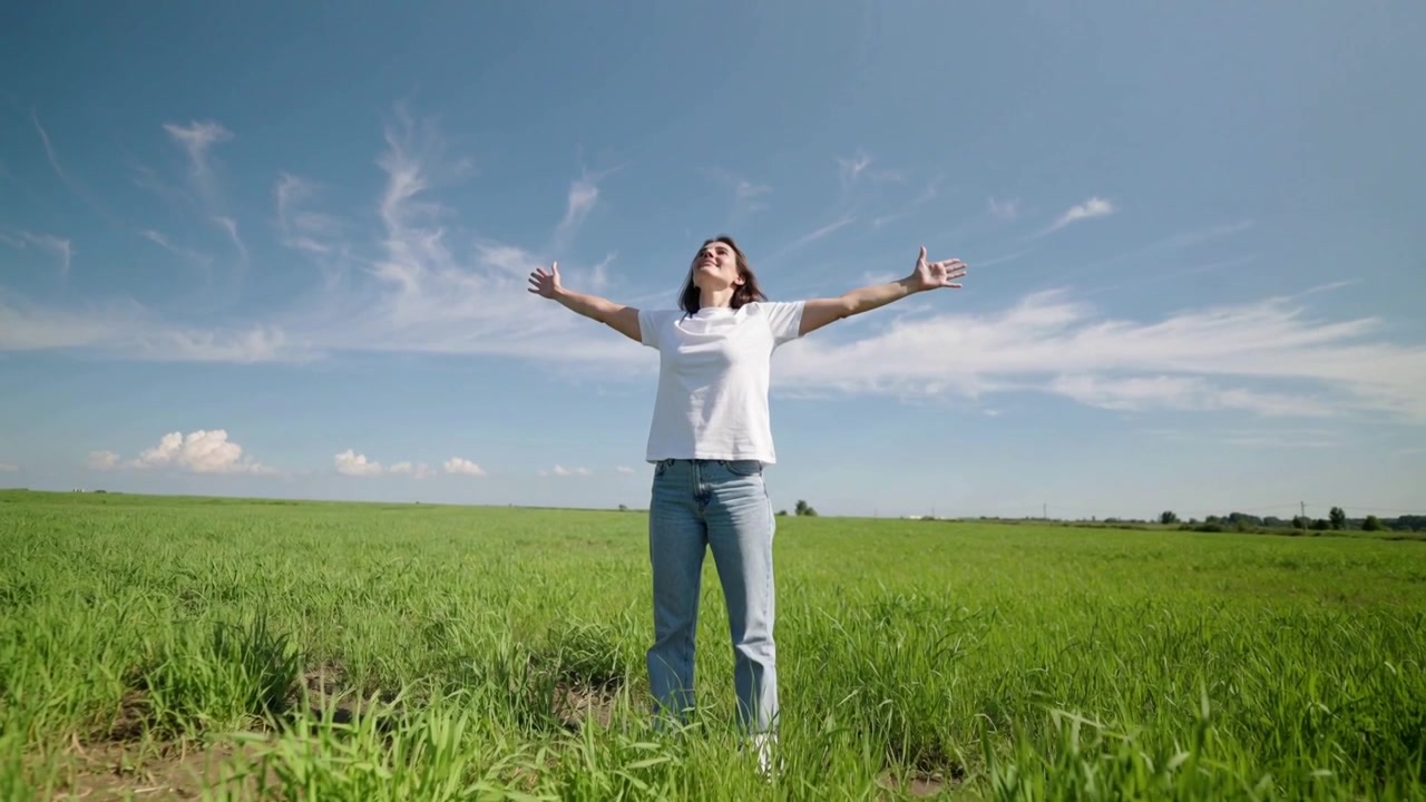 Mujer respirando profundamente, estirando los brazos hacia afuera en un campo bajo el cielo, con un accesorio de muñeca visible.
