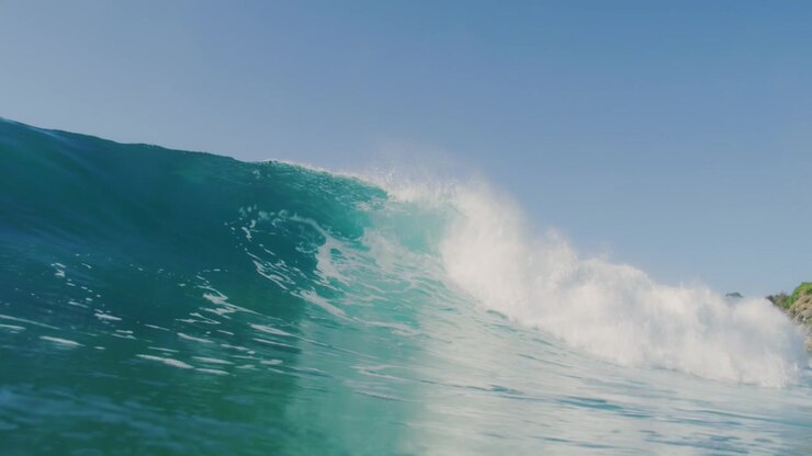 Slow-motion view of a powerful ocean wave crashing with intensity, filmed at sunrise from the water, capturing the wave's sheer force and spray