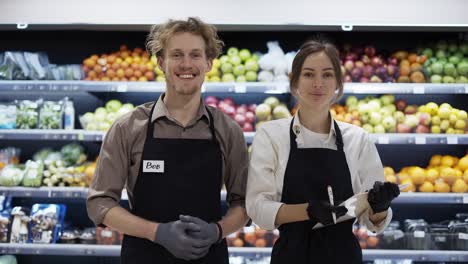 happy workers in black apron pose for the camera on the background of fruits. work in the store. weekdays. healthy food