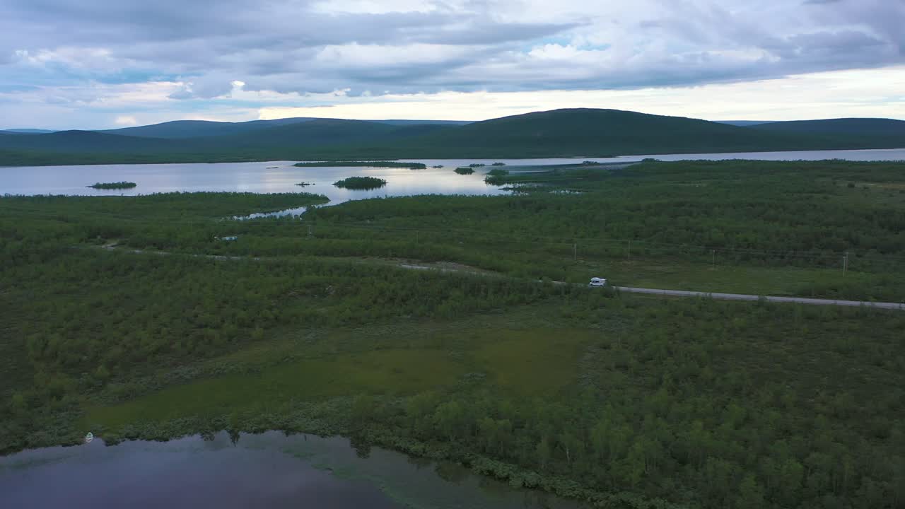 Aerial view following a RV driving in boreal wilderness, at the arctic circle dark, moody, summer evening, near Kilpisjarvi, in Enontekio, Lapland, Finland - Trucking, drone shot