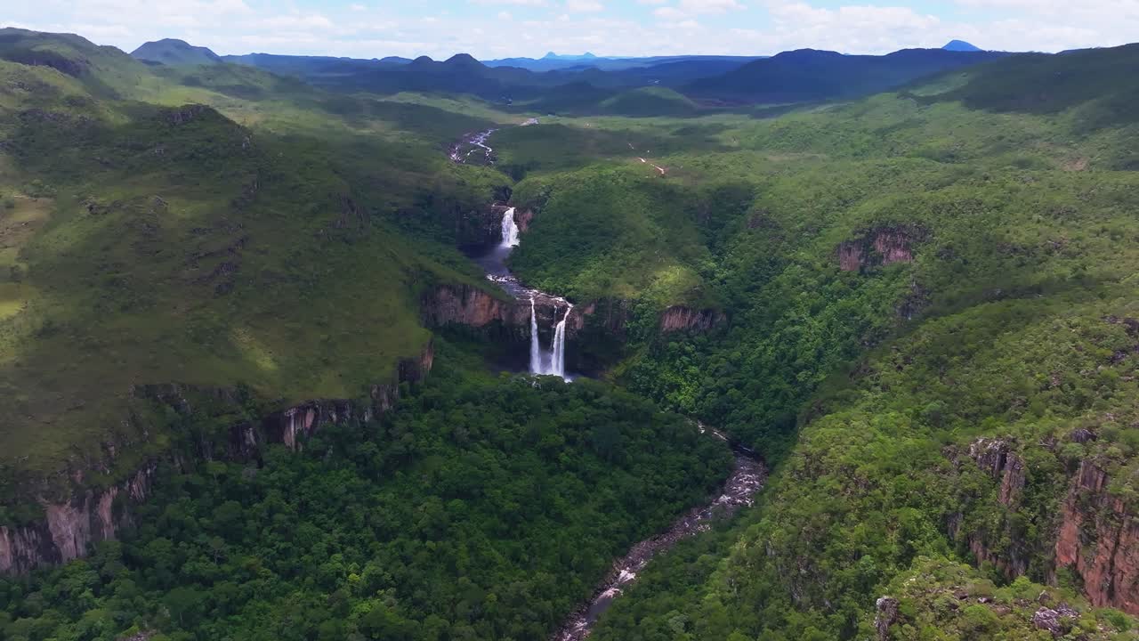 Aerial view capturing Cachoeira dos Saltos waterfall flowing through lush green vegetation in Chapada dos Veadeiros National Park, highlighting the Cerrado biome's beauty, drone establishing shot