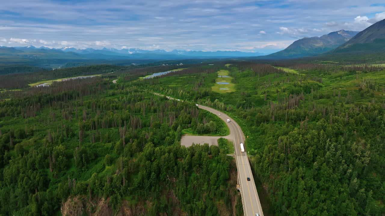 Discover Alaska serene views. Vibrant green forests stretch across the Alaskan wilderness, with winding roads and majestic mountains in the backdrop