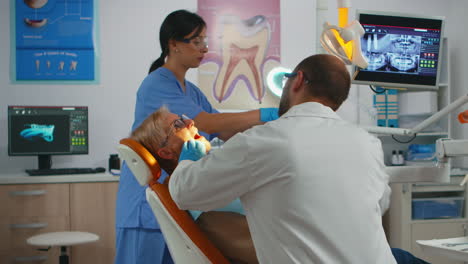 dentist working in dental unit with nurse and man lying patient
