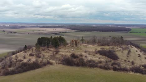 Old-ruins-on-a-hill-with-an-agricultural-landscape-and-cloudy-sky-behind,-arc-shot-right